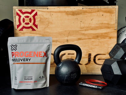 Progenex Recovery supplement package with kettlebell and dumbbells on a wooden box