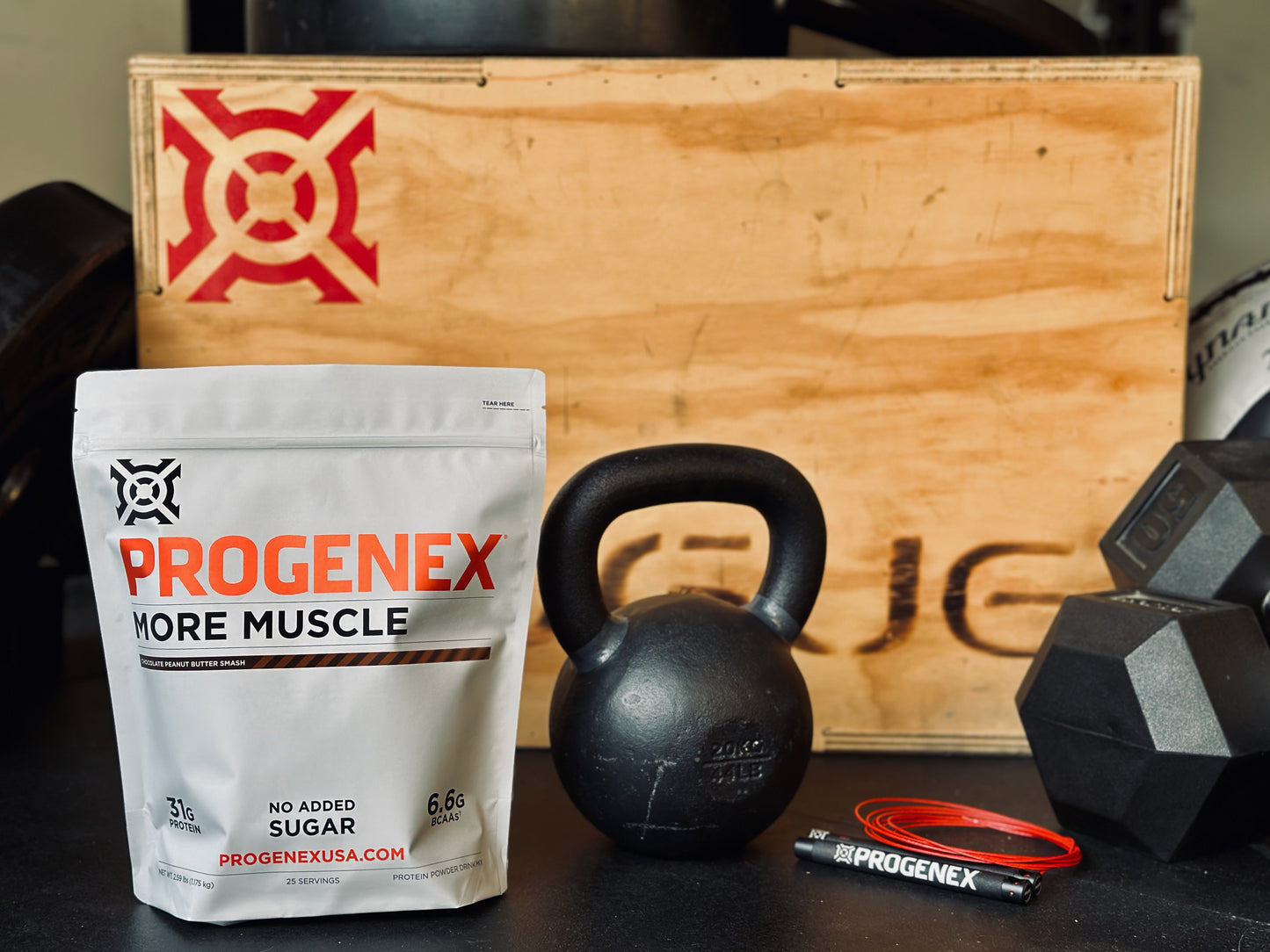 Progenex supplement package with kettlebell and dumbbells on a wooden box background