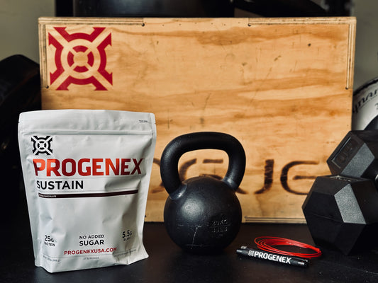 Progenex Sustain supplement package with kettlebell and dumbbells on a wooden box background